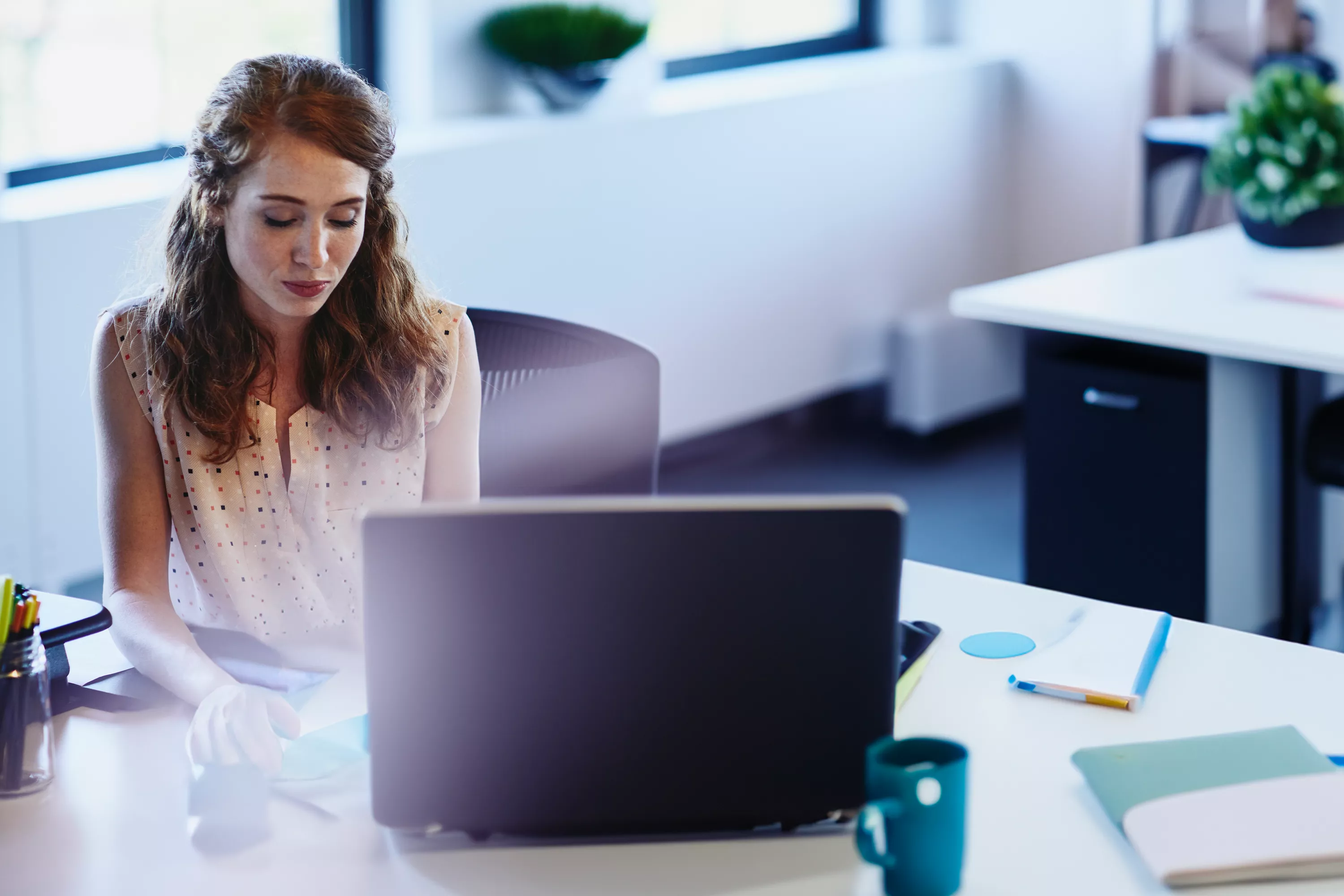 eine Frau sitzt mit nachdenklichem Blick am Schreibtisch vor ihrem Laptop