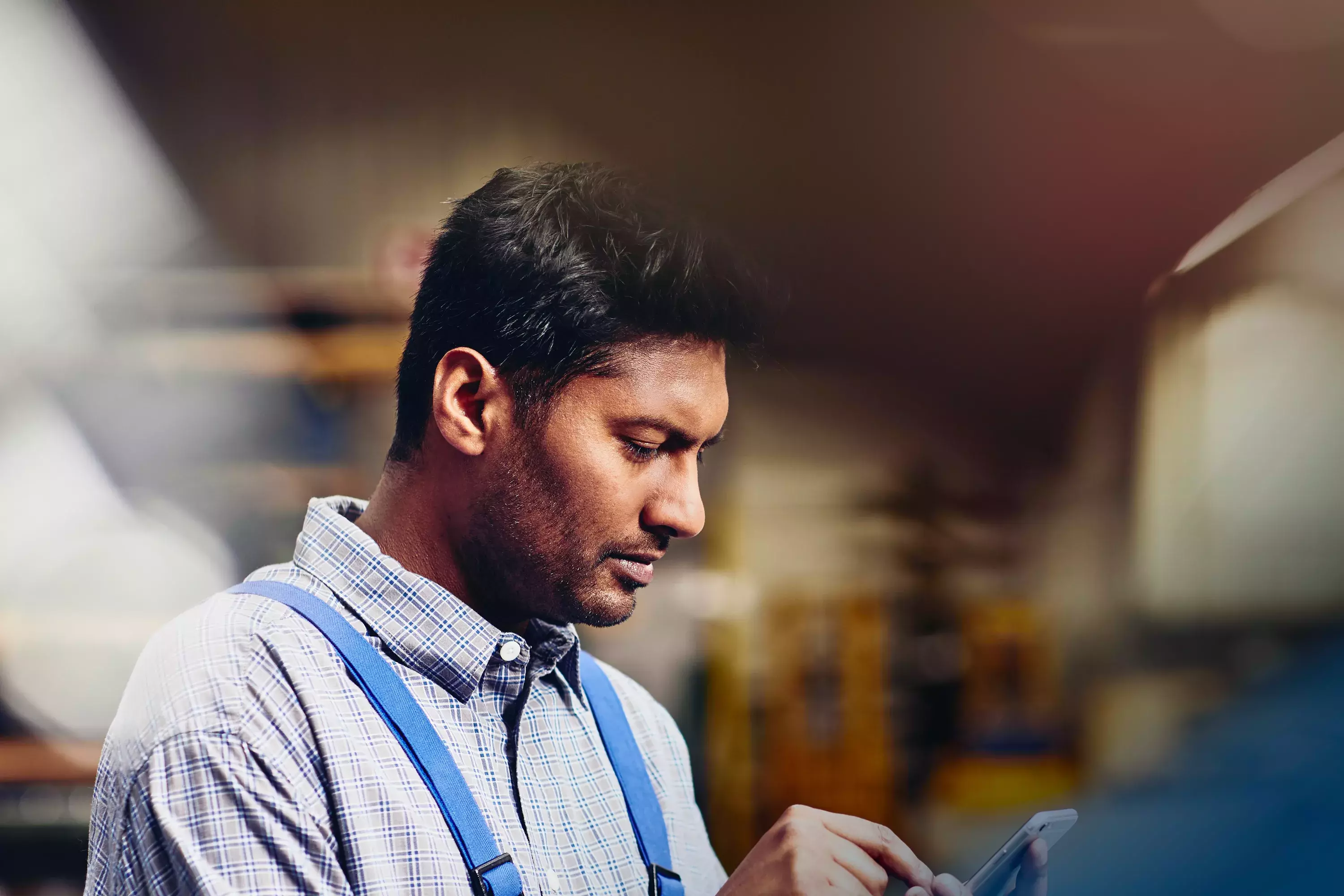 Focused male looking down to phone in production site.
